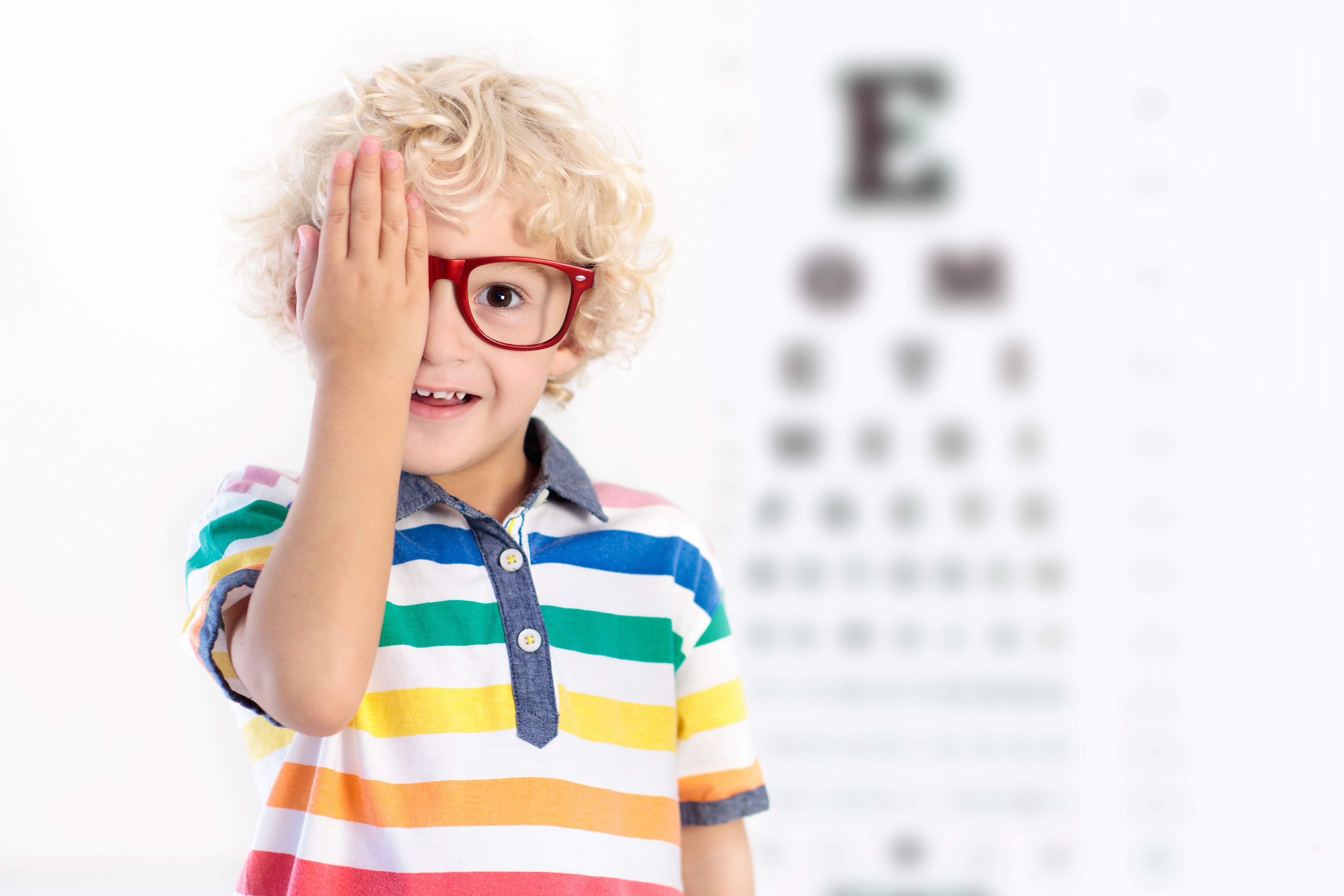 blonder Junge mit roter Brille hält sich ein Auge zu