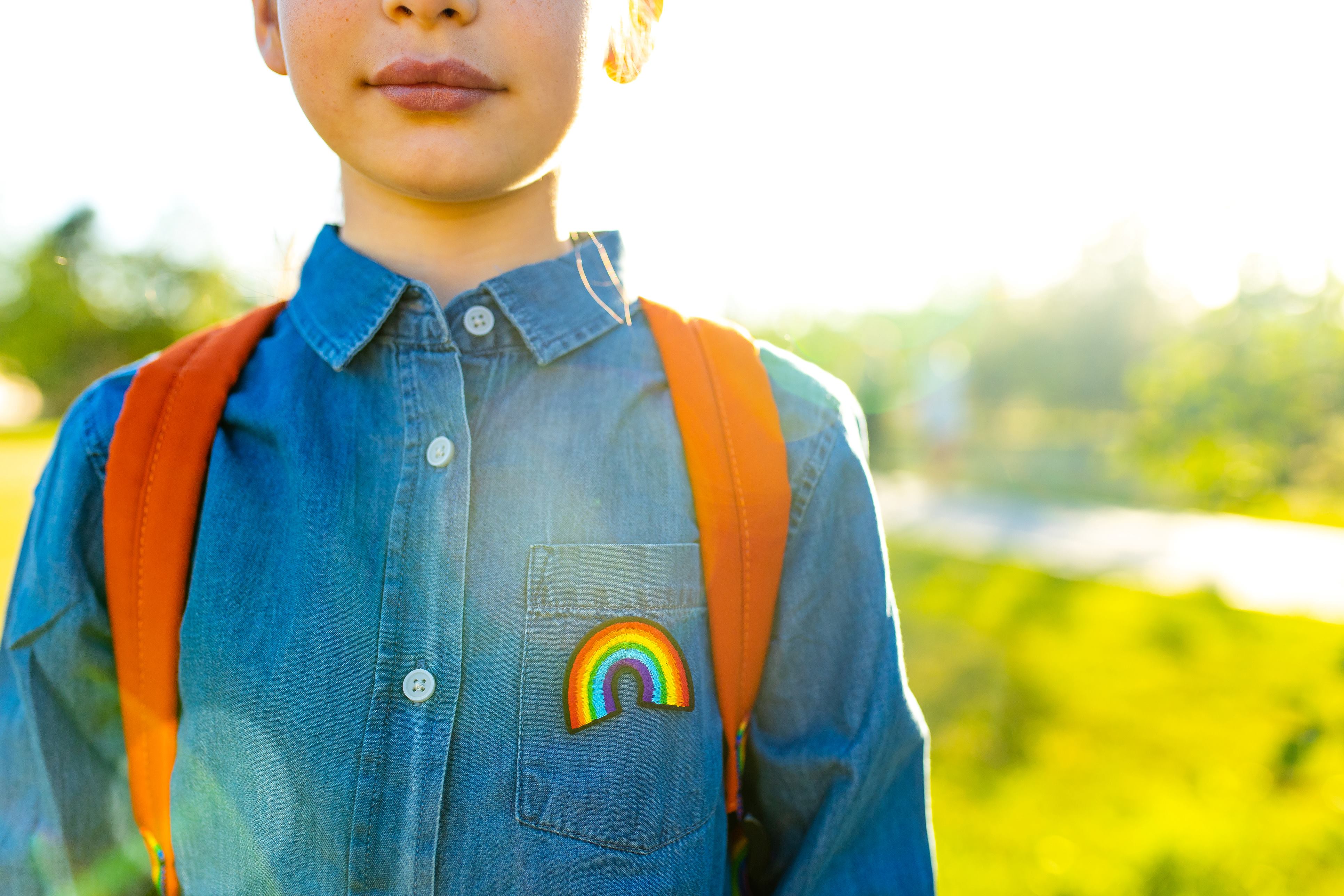 Kind mit Rucksack, Jeansjacke und einem Regenbogenanstecker
