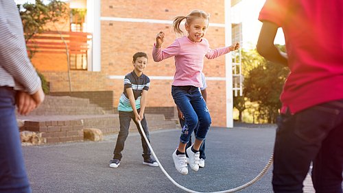 Kinder springen draußen Sringseil auf dem Schulhof