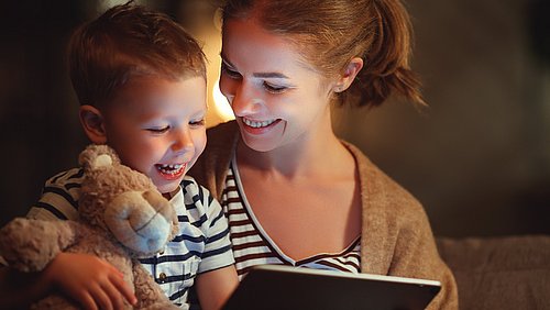 Mutter und Sohn lachen während sie etwas auf dem Tablett schauen 