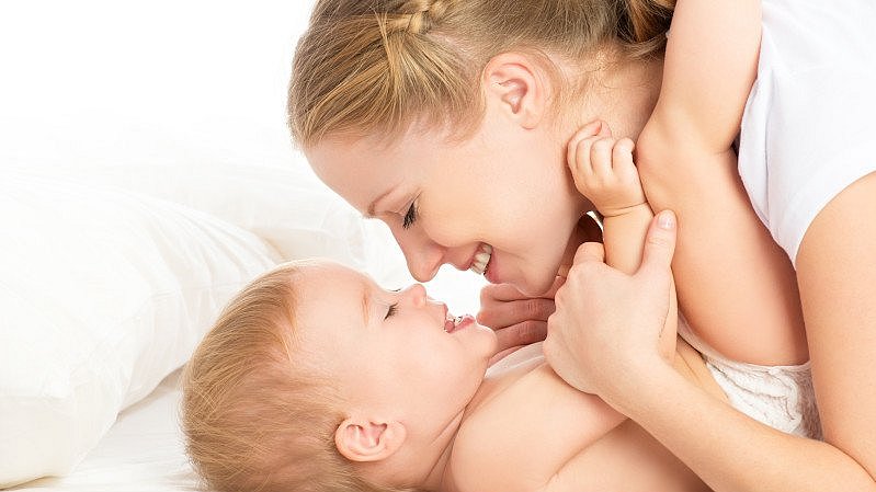 Mama und Baby kuscheln im Bett mit zugewandten Gesichtern