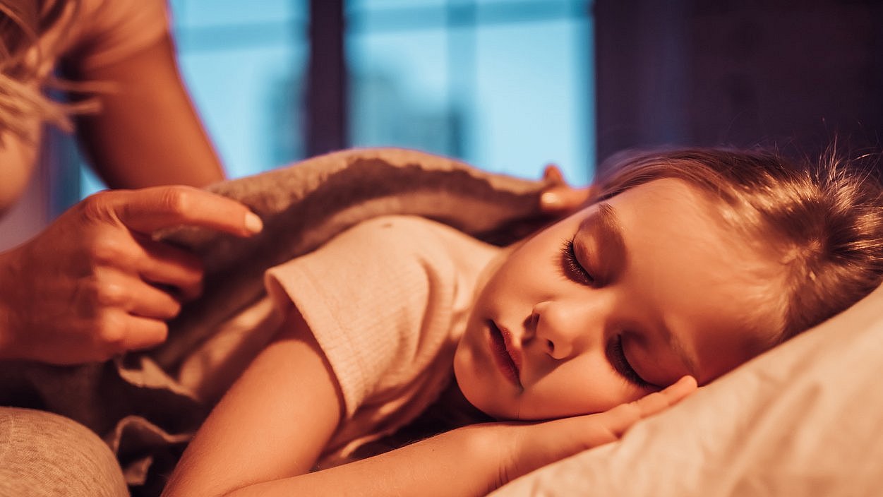 Mutter deckt schlafende Tochter im Bett zu