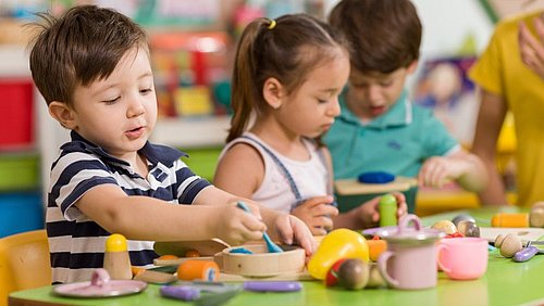 Drei Kinder spielen mit Holzbesteck und Lebensmitteln aus Holz