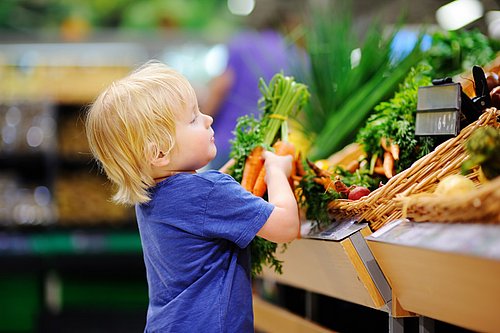 Kleiner_Junge_greift_nach_einem_Buendel_Moehren_im_Supermarkt
