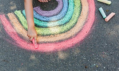 Kind malt einen Regenbogen mit Kreide auf den Boden