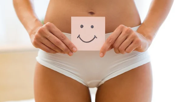 Eine Frau hält einen Post-IT Zettel mit einem Smiley for den Bauch