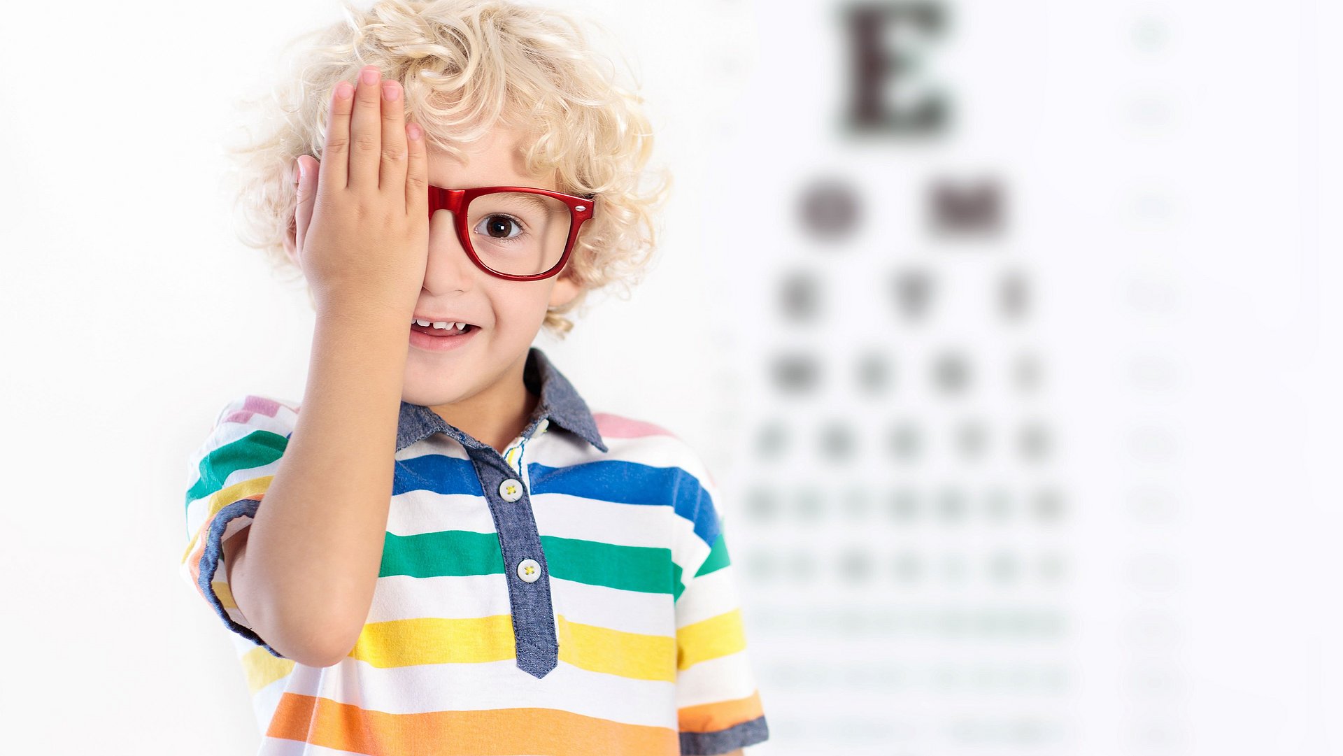 blonder Junge mit roter Brille hält sich ein Auge zu