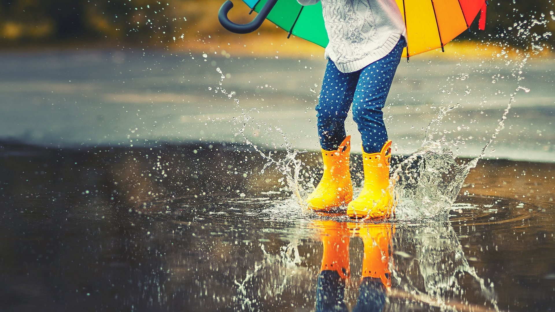 Kind draussen im Regen springt in einer Pfütze mit Gummistiefeln
