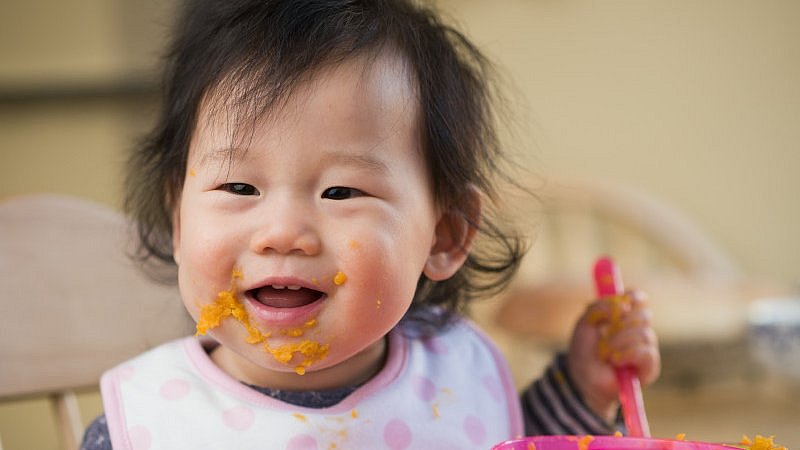 Niedliches_Baby_mit_verschmierten_Mund_und_Lätzchen-hält_Breilöffel