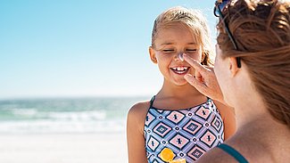 Mutter cremt am Strand Tochter ein