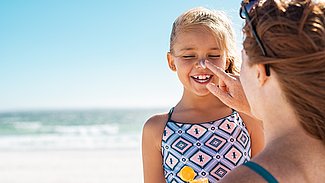 Mutter cremt am Strand Tochter ein