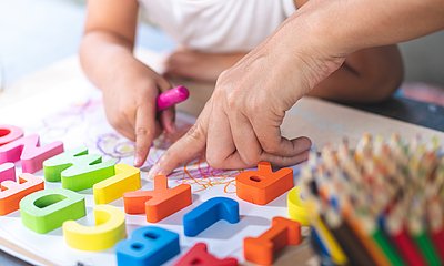 Zwei Hände zeigen auf bunte Buchstaben