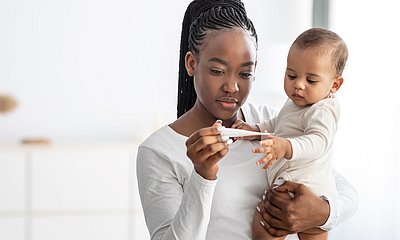 Mutter hält Kind im Arm und sie schauen gemeinsam auf ein Fiebermesser