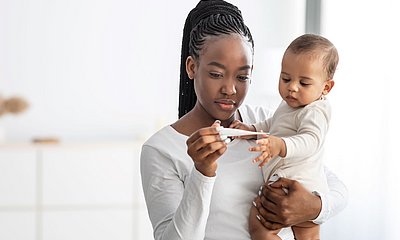 Mutter hält Kind im Arm und sie schauen gemeinsam auf ein Fiebermesser