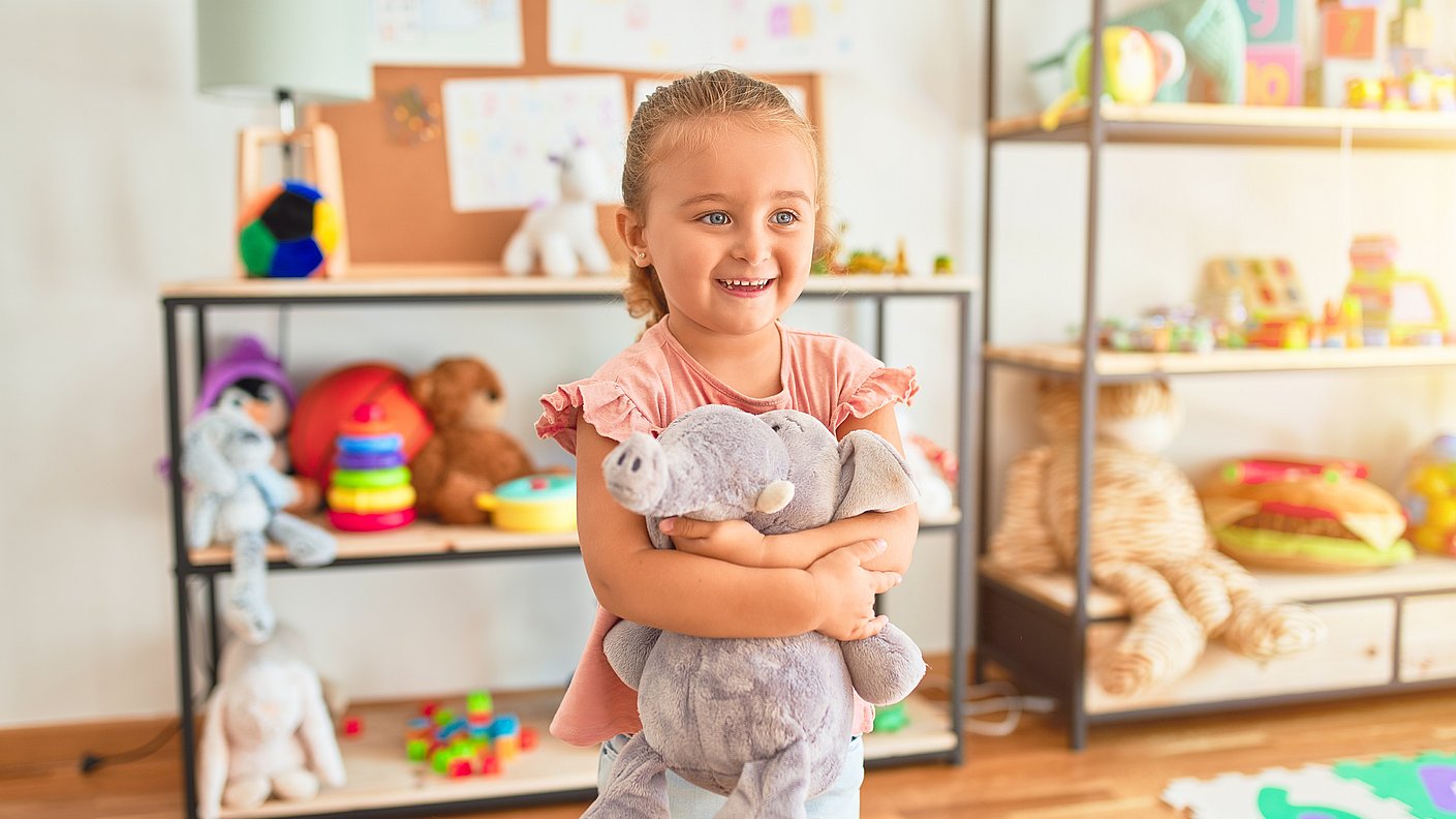 Blondes kleines Mädchen umarmt Kuscheltier Elefanten im Kindergarten