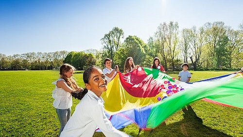Multi_ethnische_Gruppe_spielt_mit_großem_bunten_Fallschirm_gefüllt_mit_Baellen