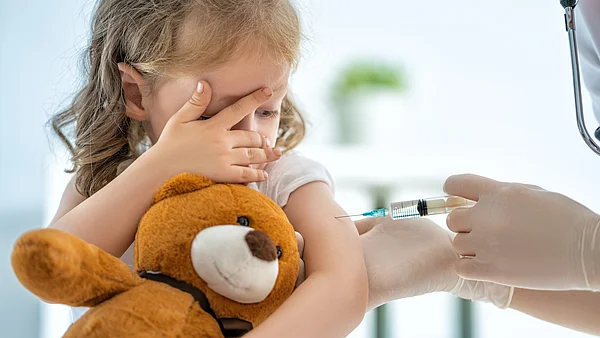 Kleines Mädchen hälte Teddy im Arm und wird geimpft