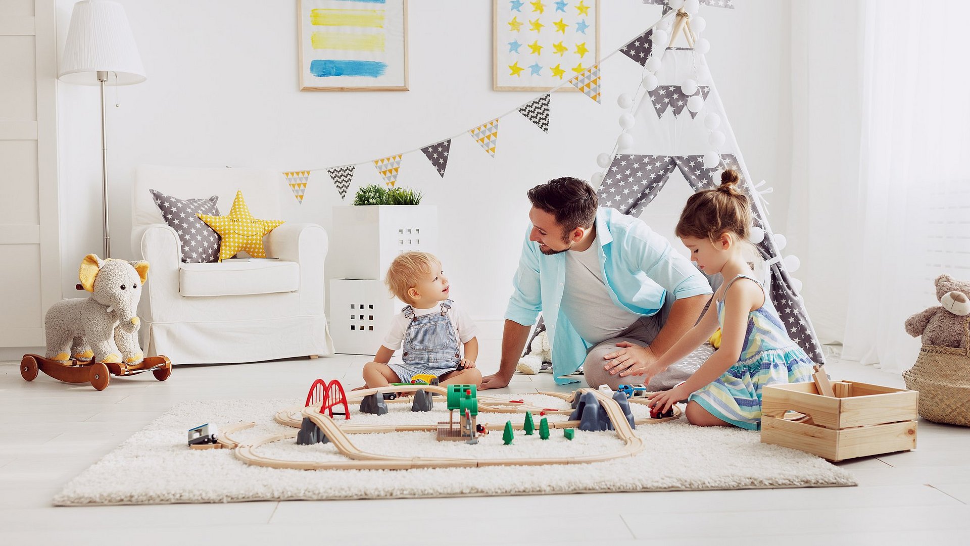 Familien Vater und seine Kinder spielen mit einer Spielzeug -Eisenbahn im Spielzimmer