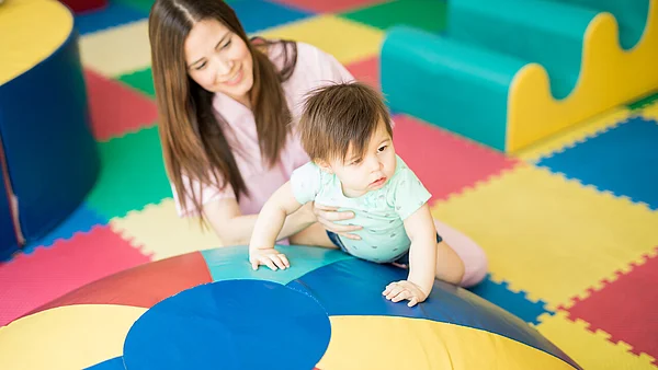 Frau hilft Kind beim bewegen auf Spielsachen