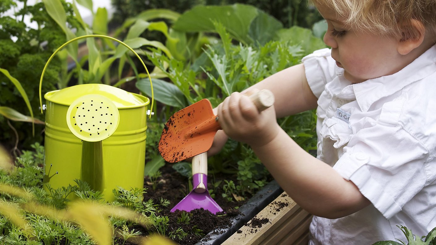 Kleiner Junge spielt im Garten mit Gießkanne und Schaufel