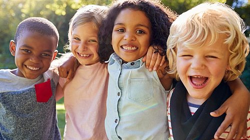 Multi_ethnische_Kindergruppe_steht_arm_in_arm_und_lächelt