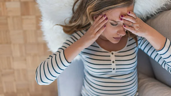 Schwangere Frau hält sich die Hände an den Kopf und verzieht da Gesicht