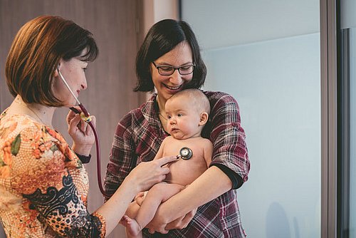 Medizinische_Fachperson_untersucht_Baby_im_Arm_der_Mutter