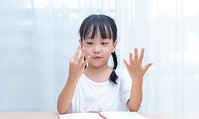 Kind sitzt am Pult und zählt mit den Fingern