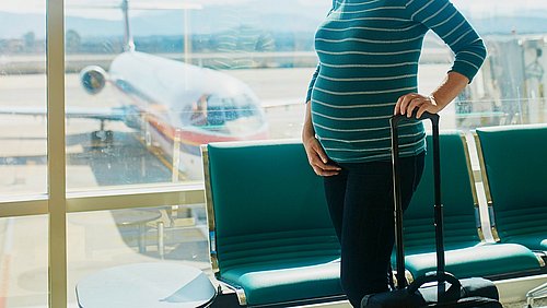 Schwangere Frau am Flughafen mit ihrem Koffer