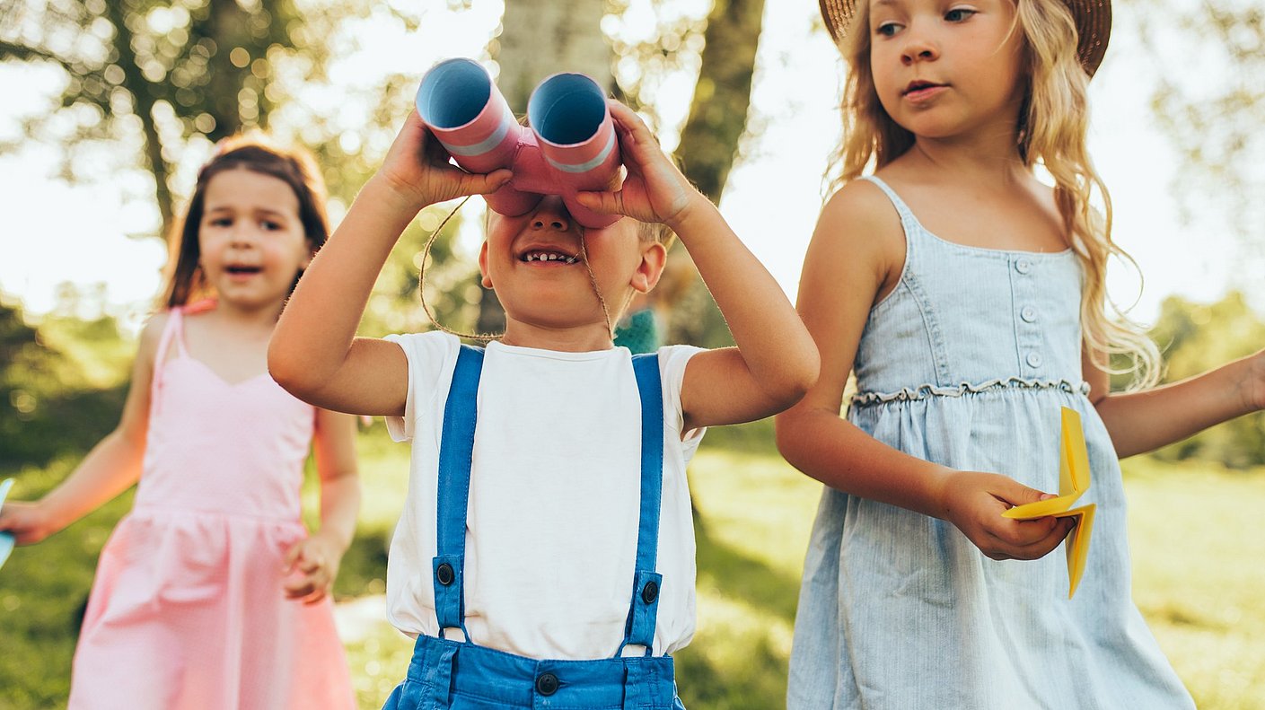 Kinder spielen mitFernglas und Papierflugzeug draußen