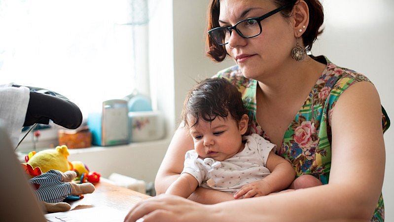 Mutter_arbeitet_am_Laptop_mit_Baby_im_Arm