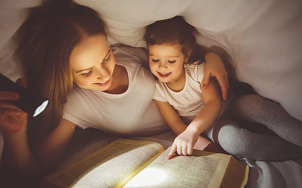 Mutter und Tochter lesen unter der Bettdecke