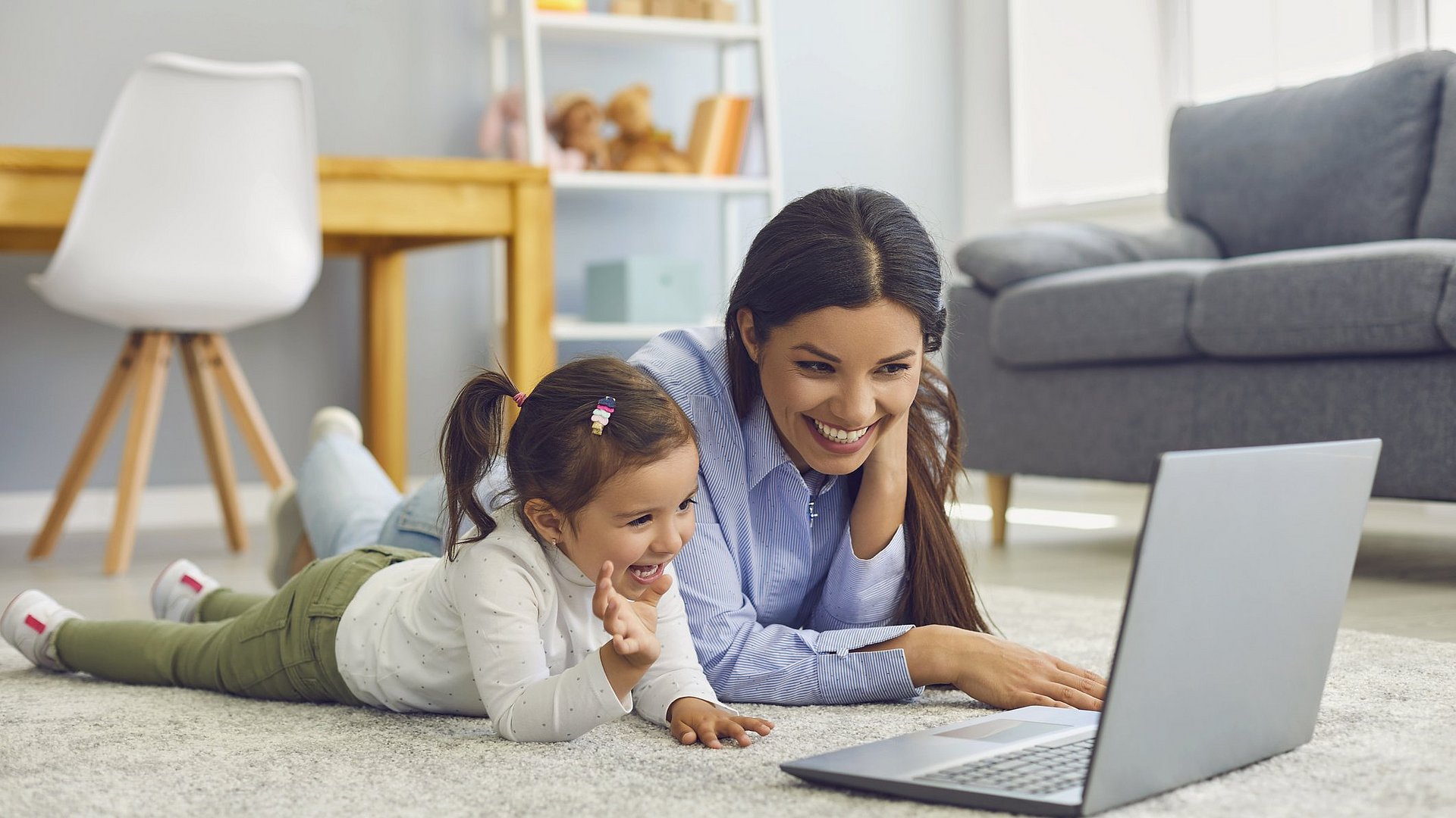 Mutter und Tochter liegen am Boden und schauen etwas auf dem Laptop 