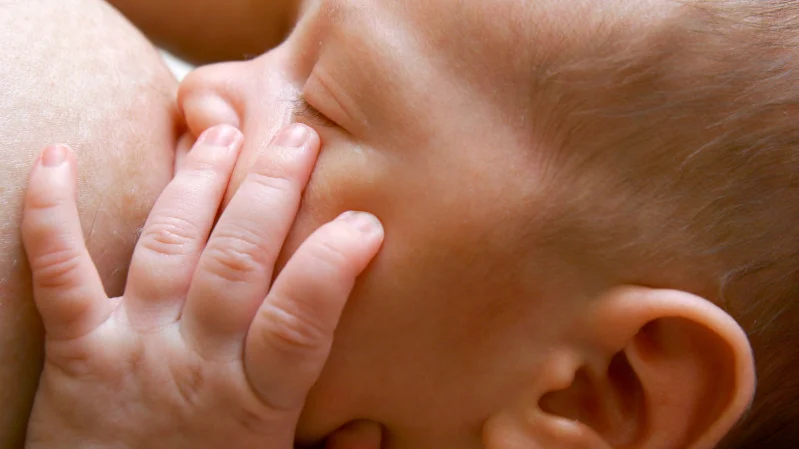 Baby saugt an der Brust und hält Hand an das Gesicht