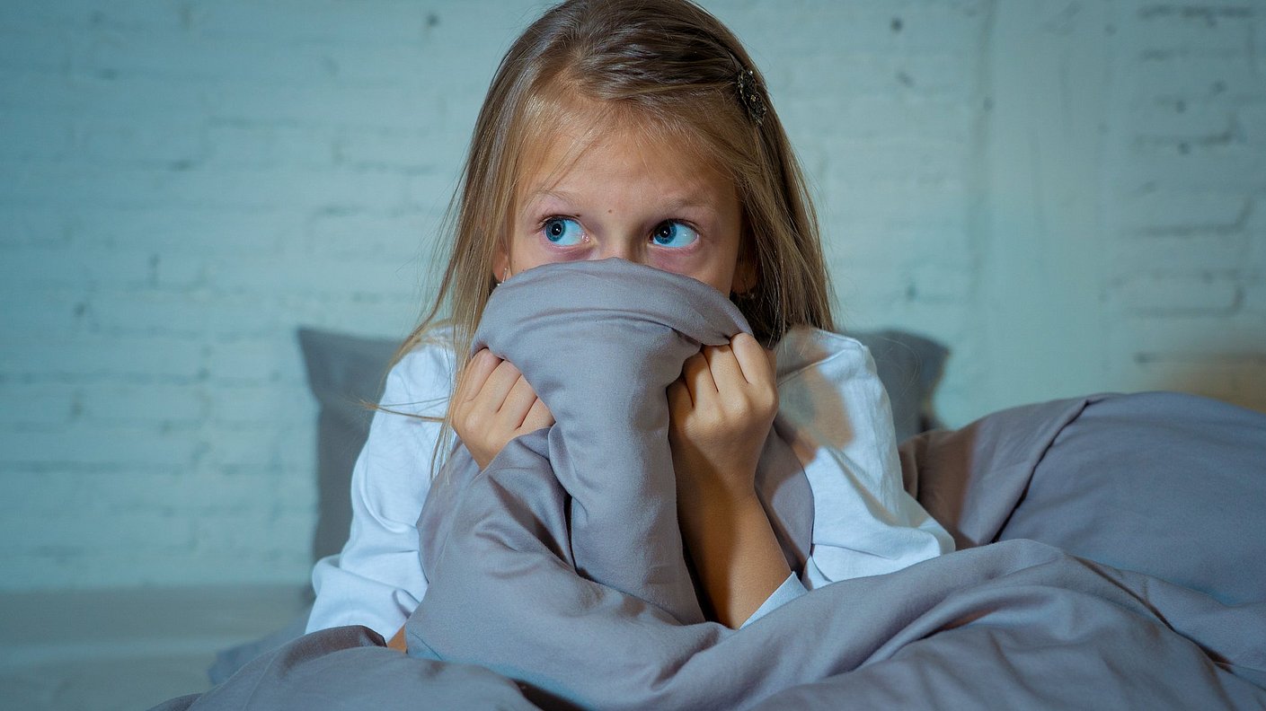 Kleines Mädchen versteckt sich ängstlich hinter ihrer Bettdecke 