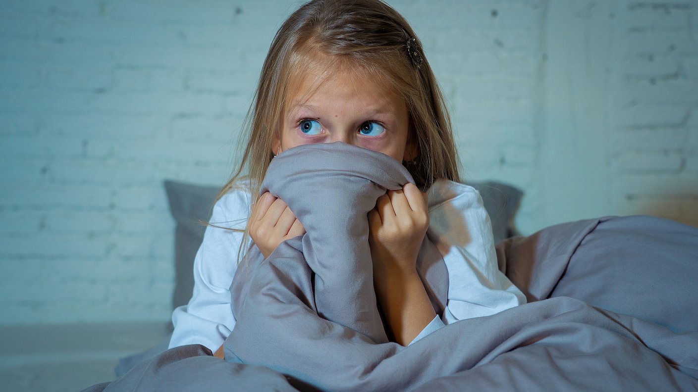 Kleines Mädchen versteckt sich ängstlich hinter ihrer Bettdecke 