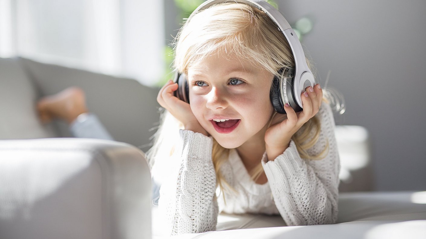 Glückliches kleines Mädchen liegt auf dem Sofa und hört mit Kopfhörern Musik