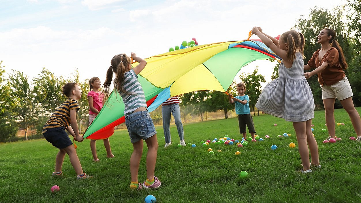 Kinder spielen auf einer Wiese mit einem bunten Fallschirm