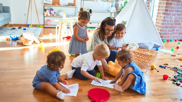 Lehrerin und kleinkind Gruppe sitzen mit Papier und Buntstiften auf dem Boden