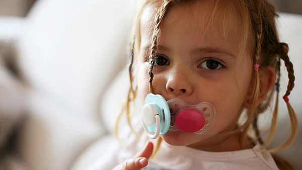 Mädchen mit geflochtenen Haaren hat zwei Schnuller im Mund