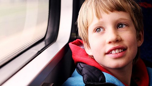 Junge_mit_rotem_Pullover_und_blauer_Jacke_schaut_aus_Fenster