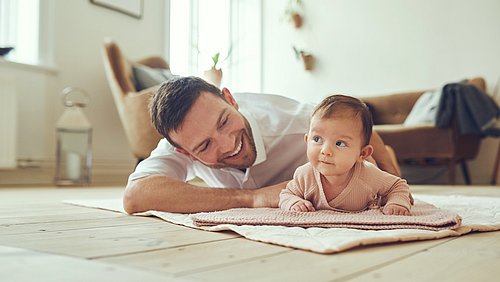 Lächelnder Vater liegt mit seiner Baby Tochter auf dem Boden