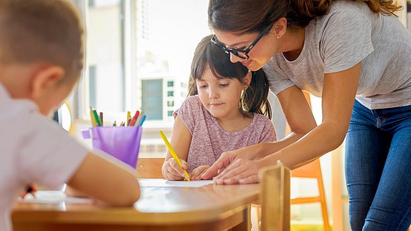 Lehrerin Arbeitet mit zwei Kindern an einem Schultisch