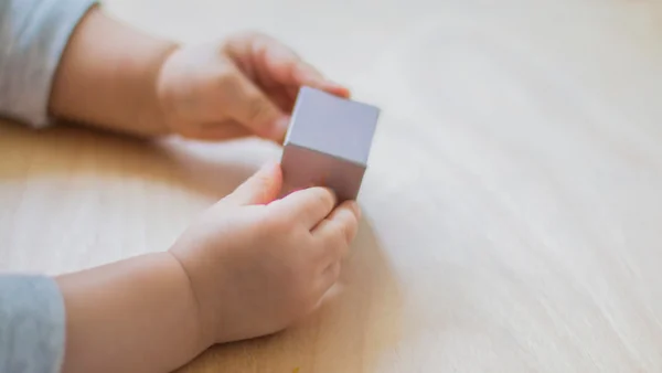 Kleine Hände halten einen viereckigen Würfel