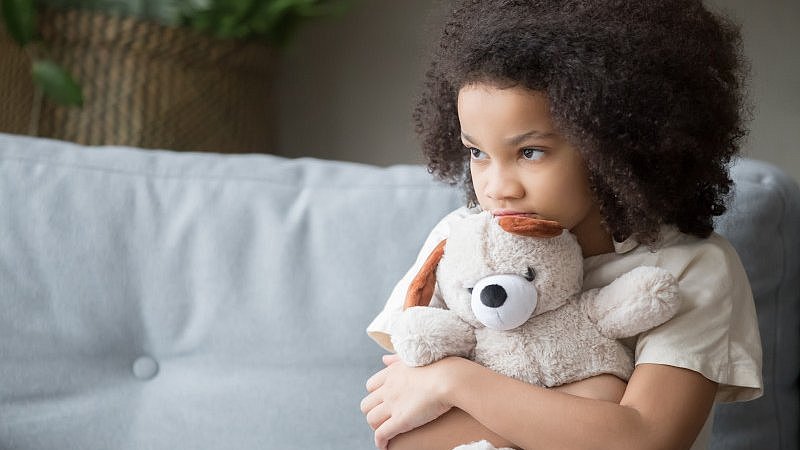 Mädchen_sitzt_auf_weißem_Sofa_und_umarmt_Teddybär