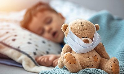 Schlafender Junge mit einem Teddy, der eine Maske aufhat