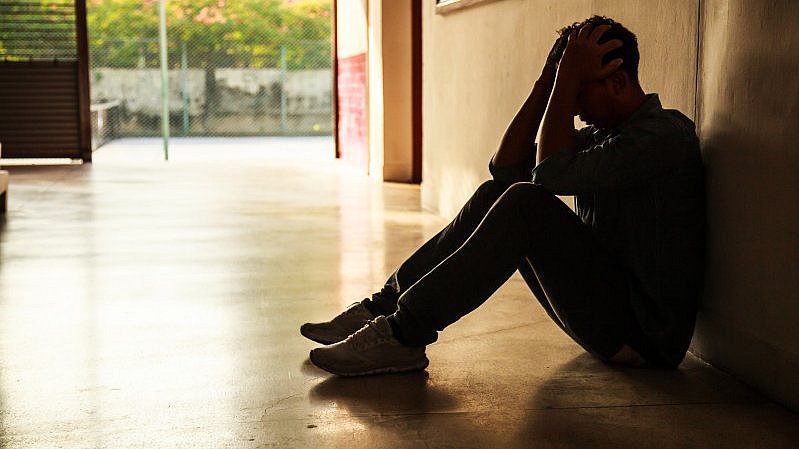Person sitzt im Halbdunke auf dem Boden und hält sich den Kopf
