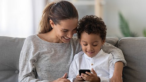 Mutter und Sohn sitzen zusammen auf dem Sofa und schauen auf ein Handy 