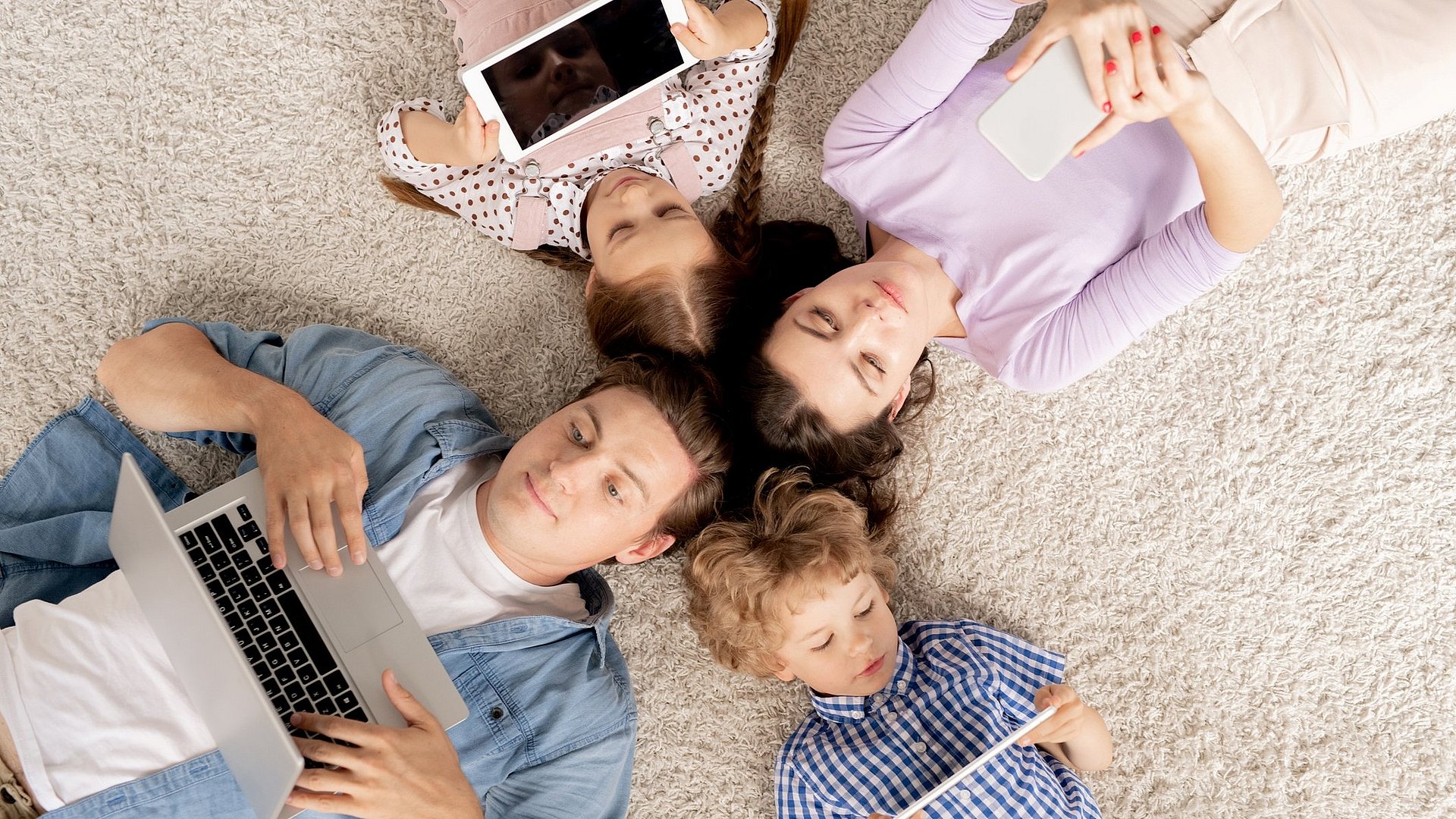 Top-Ansicht einer Familie aus vier Personen die alle an mobilen Geräten sind 