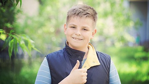 Junge in blauer Jacke zeigt Daumen hoch Geste